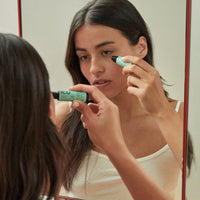 Woman applying eye serum in front of a mirror