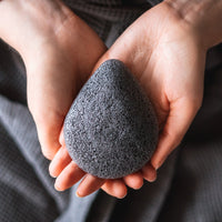 Person holding a black konjac sponge between their fingers.