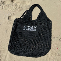Black woven bag with 'G'DAY GORGEOUS' text on sand